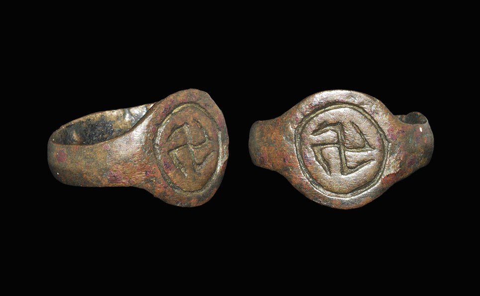 Roman Bronze 'Swastika' Ring: 2nd-3rd century AD. A cast ring with carinated hoop, discoid bezel and intaglio with 'gammadion' motif. 3.93 grams, 21 mm overall, 17.33 mm internal diameter (approximate size British N 1/2, USA 6 3/4