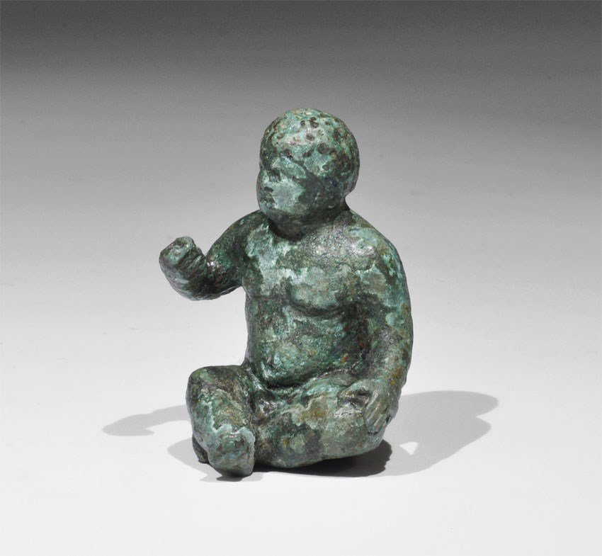 Roman Bronze Seated Infant Hercules Figurine: 1st-2nd century AD. A cast model of Hercules as a baby, seated nude with left hand on his knee, right hand raised. 149 grams, 53 mm (2"). UK art market, acquired prior to 1980.