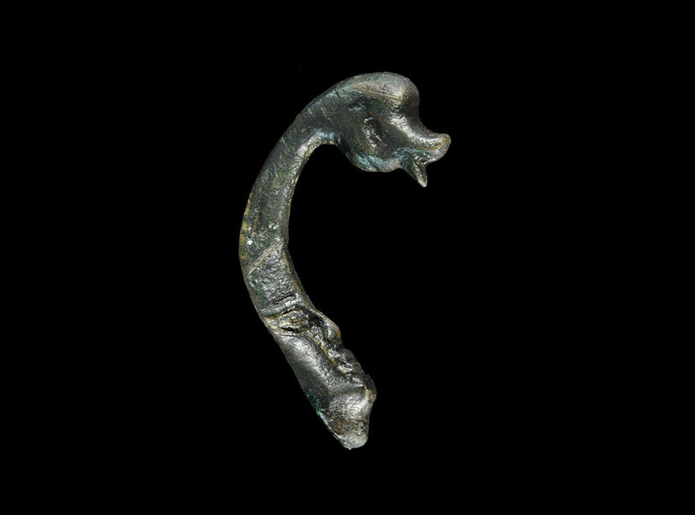 Roman Bronze Bowl Mount with Face-and-Duck Hook: 1st-2nd century AD. A cast mount with hook below, modelled with a human mask on the ovoid upper section, bird-head terminal to the hook. 27 grams, 55 mm (2 1/4"). Property of a Nottinghamshire gentlem
