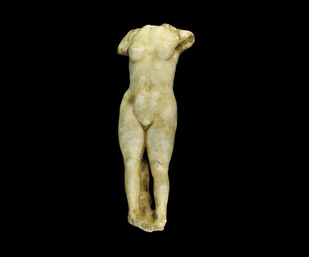 Roman Marble Torso of Venus: 1st-2nd century AD. A fine quality carved figurine of Venus standing nude, the trunk of a tree behind her right leg; the lower section of her hair resting on the shoulders and back, the left shoulder 