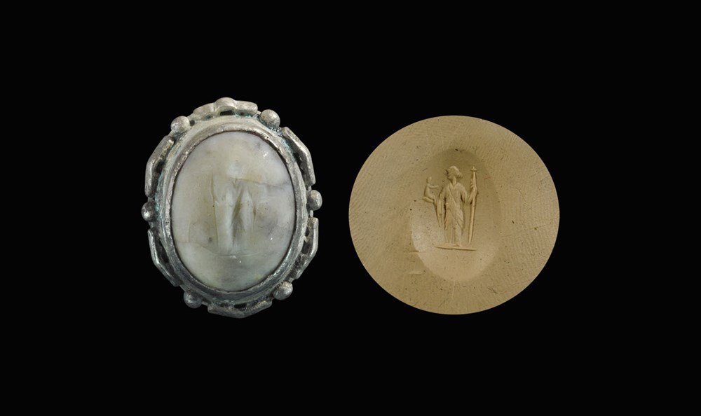 Roman Marble Silver-Mounted Intaglio: 1st-2nd century AD. A domed insert in a silver frame with segmented band, intaglio insert with standing robed figure with staff and child. 9.50 grams, 29 mm (1 1/4"). UK art market, acquired prior to