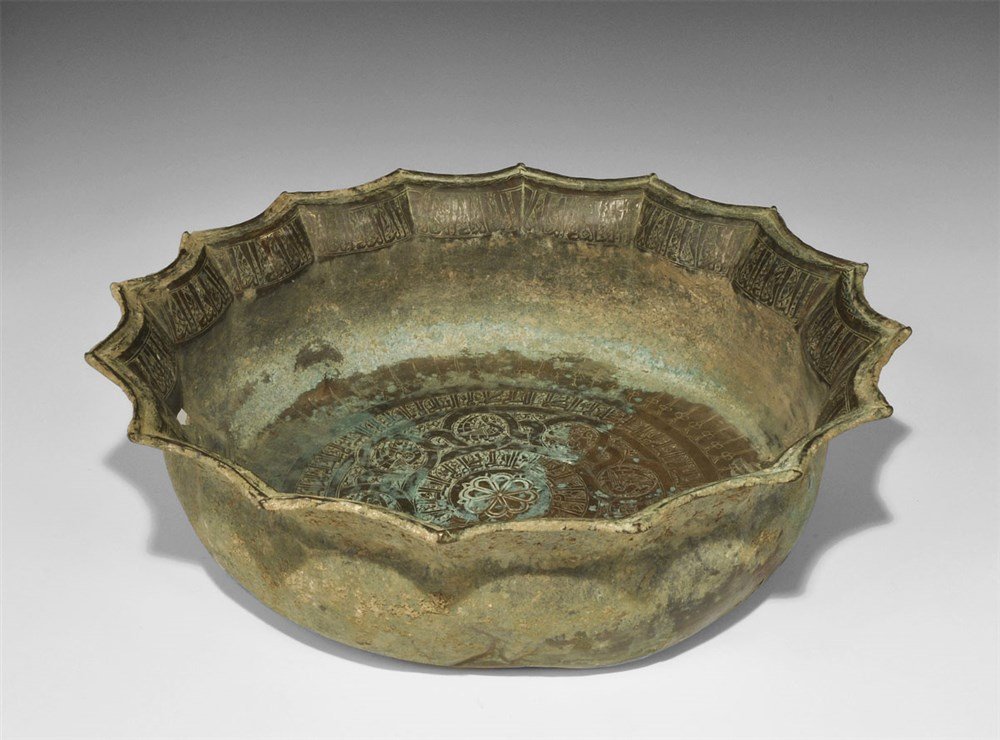 Islamic Khorasan Bronze Calligraphic Bowl: 12th-13th century AD. A sheet-bronze bowl with fluted rim; two bands of calligraphic text to the inner face with birds in panels and central rosette; calligraphic text to the rim. 1.7 kg, 43 cm (17").