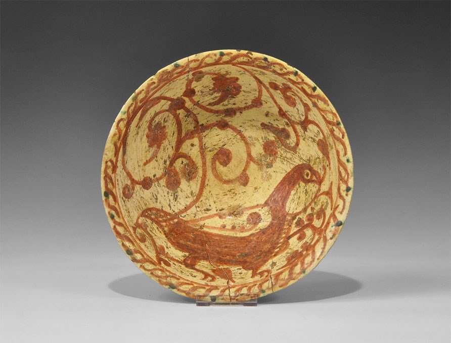 Islamic Khorasan Ceramic Bird Painted Bowl: Samanid Dynasty, 819-999 AD. A yellow-glazed bowl with basal ring and everted rim; the outer face ornamented with concentric rings in red, the inner face with a red bird amid scrolled foliage, guilloc