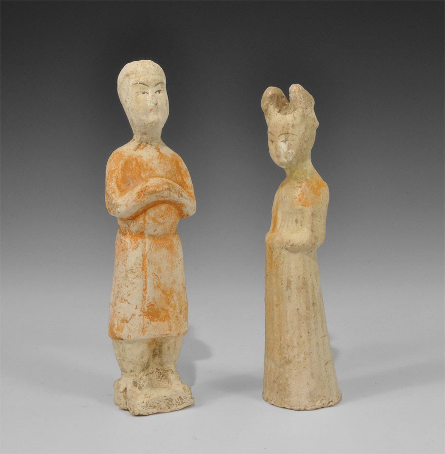 Chinese Ceramic Female Attendant Statuette Pair: Han Dynasty, 206 BC-220 AD. A group of two attendant figurines comprising: one hollow-cast, in floor-length robe with hands folded at the midriff; one in riding coat and boots, hands folded at the che