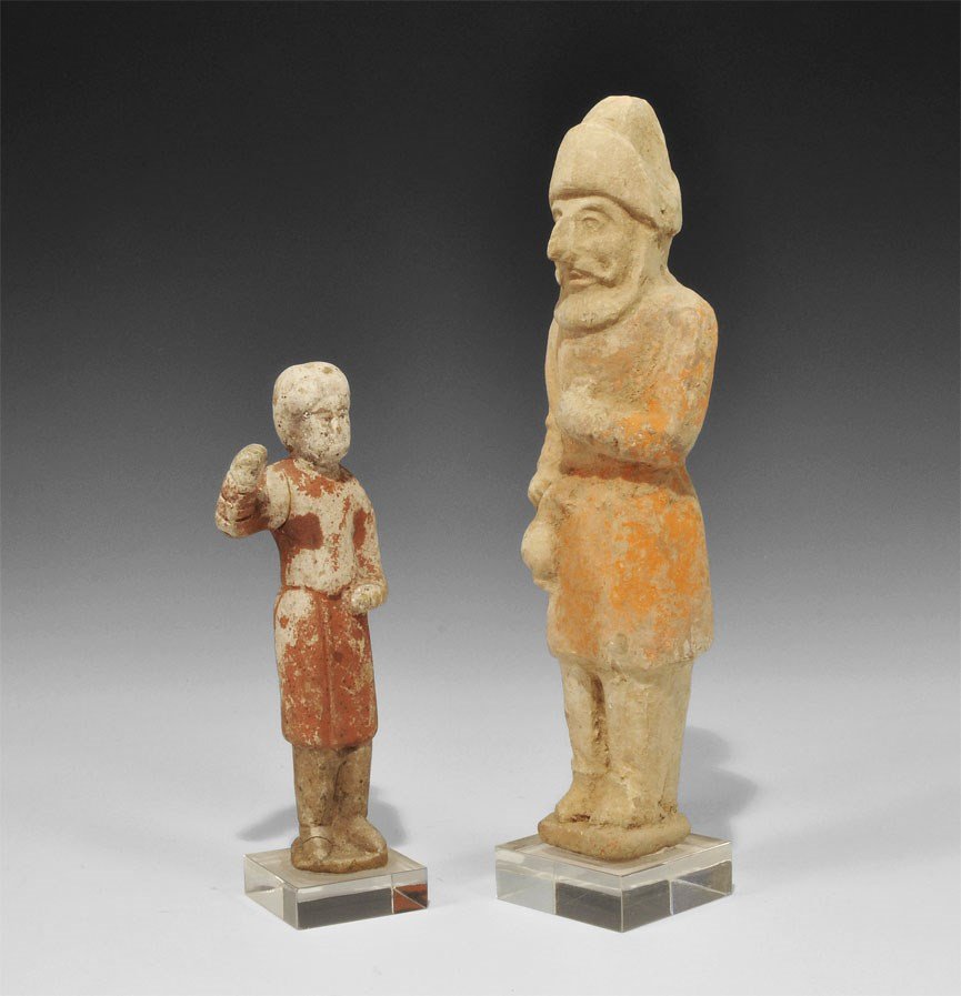 Chinese Ceramic Attendant Statuette Pair: Han Dynasty, 206 BC-220 AD. A mixed group of figurines comprising: a tall bearded male in cap and riding coat holding a jar; a slender male in knee-length tunic, right hand raised; each mounted on a c