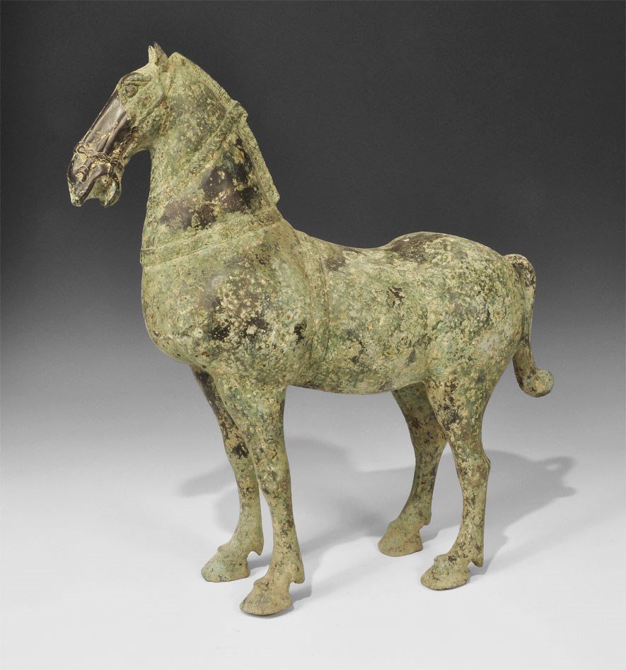 Chinese Bronze Standing Horse Statuette: Han Dynasty, 206 BC-220 AD. A cast statuette of a standing horse with bridle and harness, mouth open to accept reins; hollow to the underside. 6.3 kg, 46 cm (18"). Acquired on the London art market in