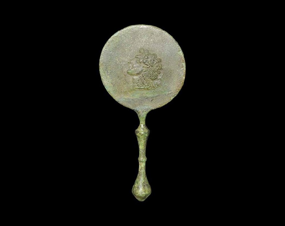 Roman Style Bronze Mirror: An undated archaistic cast mirror with discoid plaque and balustered handle; raised profile bust to reverse of the plaque. 236 grams, 20 cm (7 3/4"). Private collection, Buckinghamshire, UK; formed in