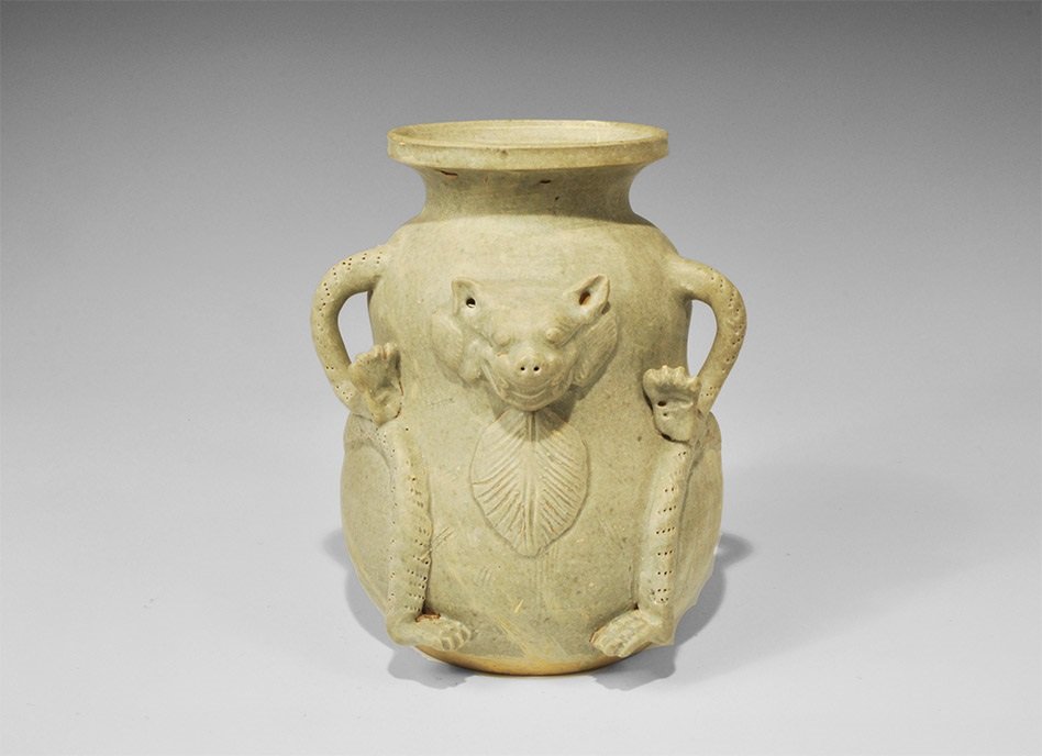 Cambodian Style Glazed Ceramic Feline Vessel: An undated archaistic green-glazed waisted vase with broad neck and flange rim; to the body, the head, tail and limbs of a feline with leaf appliqué beneath the head. 2.3 kg, 23 cm (9"). Ex South Lon