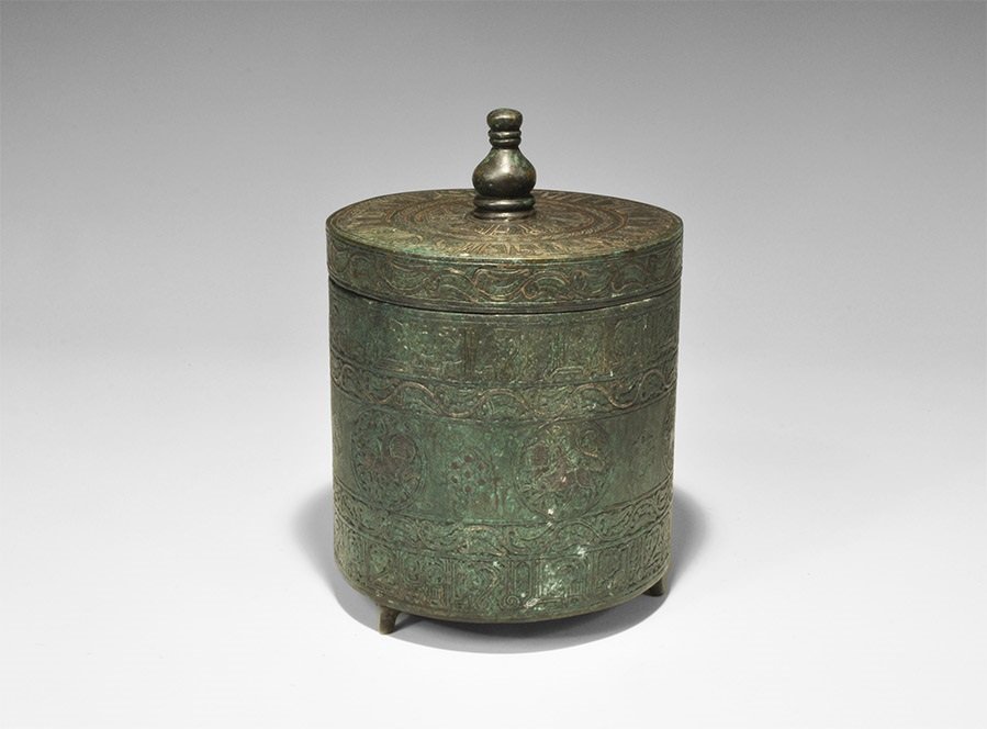 Islamic Style Bronze Calligraphic Lidded Caddy with: An undated archaistic cylindrical caddy with discoid lid; bands of silver-inlaid calligraphic text to the body and upper face of the lid, silver-inlaid running foliage to the lid and body, silver-inla