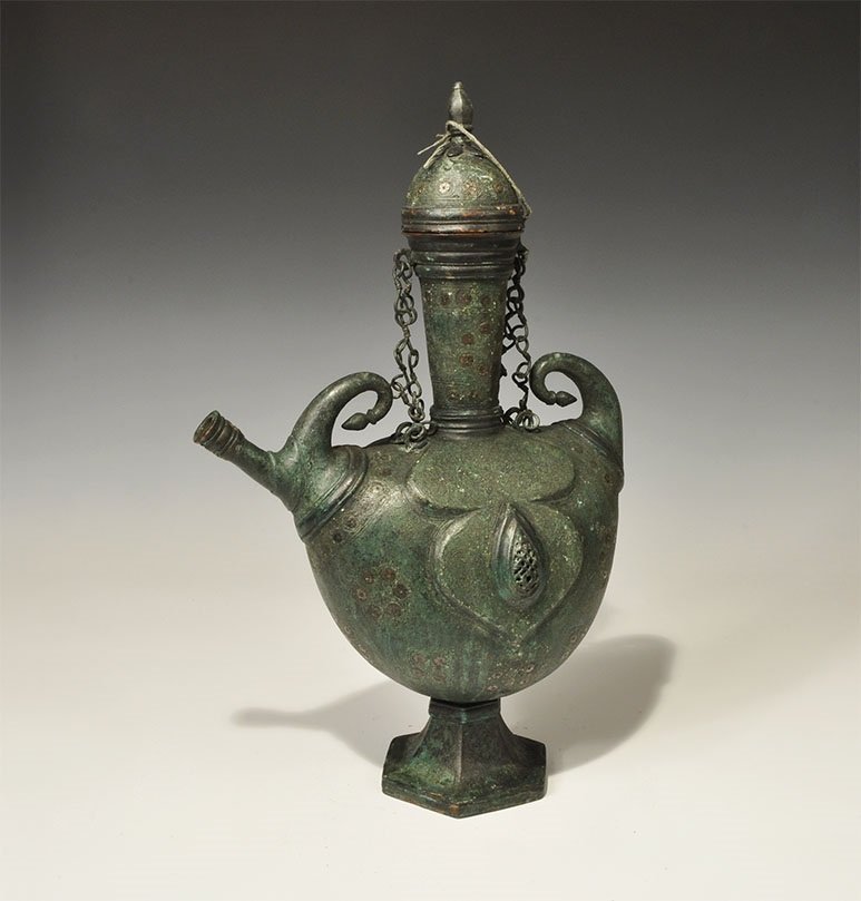Islamic Style Bronze Calligraphic Ewer with Silver: An undated archaistic ewer with bulbous body, two curled knop finials, hexagonal-section base, tubular neck with four attachment chains and and domed lid; the body with repoussé panels and openwork t