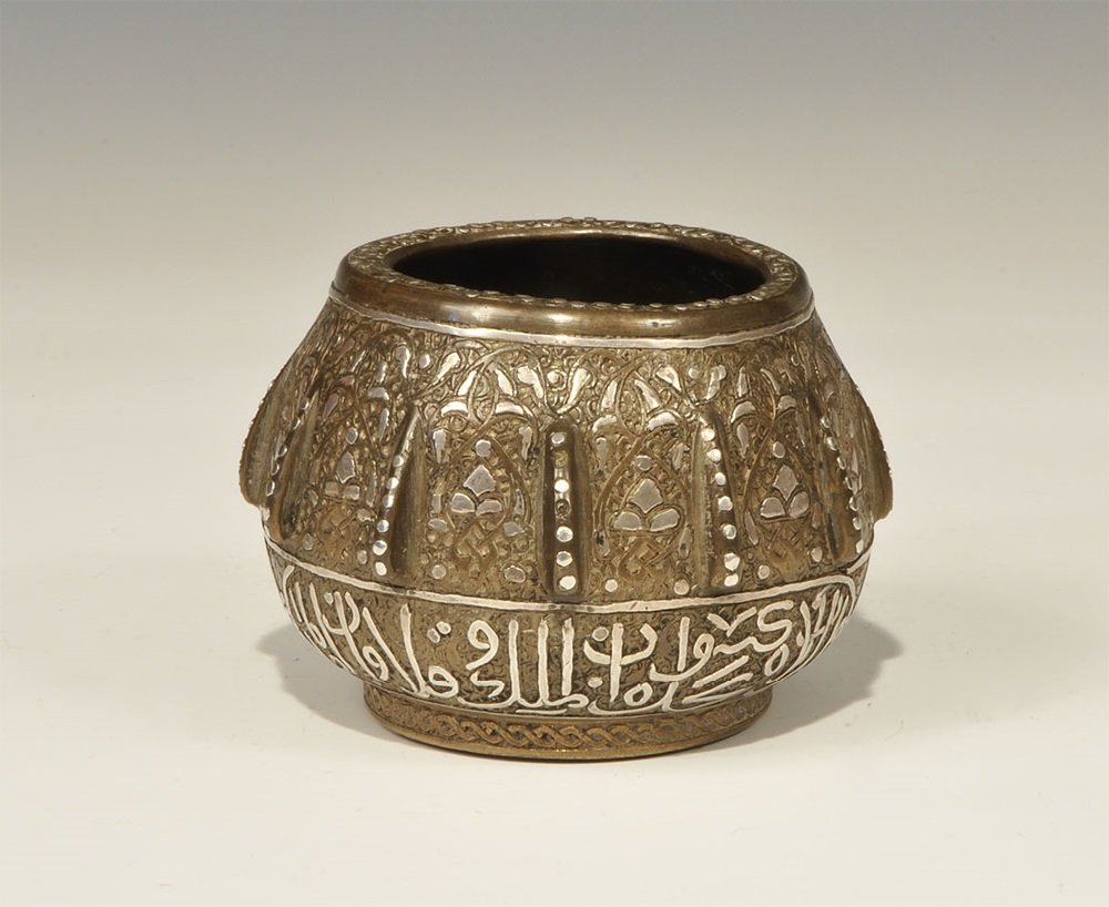 Islamic Bronze Silver-Inlaid Calligraphic Bowl: 19th century AD or later. A globular bowl with broad base, thickened rim and twelve flanges to the shoulder; the rim and flanges with inlaid studs, the shoulder with silver-inlaid foliage, the lower b