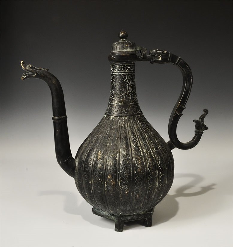 Indian Bronze Coffee Pot: 20th century AD. A cast coffee pot with bulbous body, hexagonal base with four stub legs, conical neck with domed lid, curved spout and handle; the body with vertical fluting, scrolled foliage designs