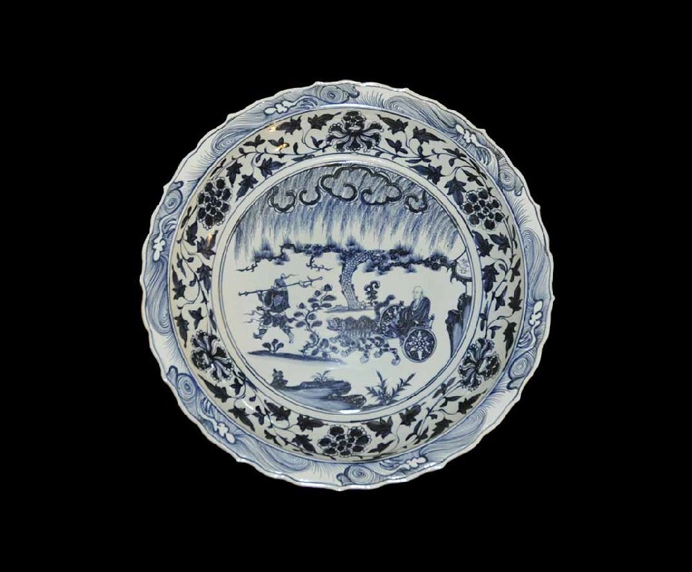 Chinese Style Ceramic Charioteer Dish: An undated archaistic blue-glazed broad dish with scrolled rim, central scene of a seated figure in a two-wheeled chariot dawn by lions preceded by an armed warrior with a halberd among vegetation and