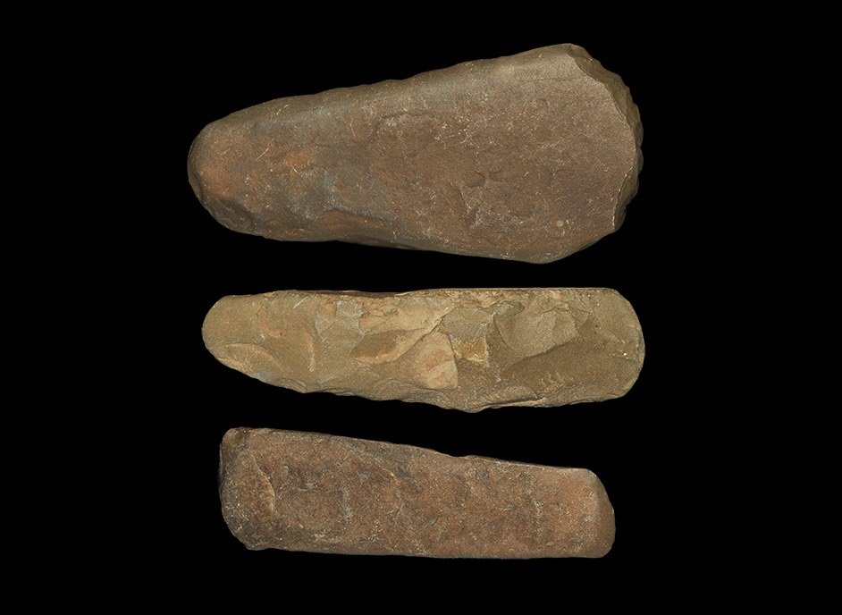 Stone Age Saharan Stone Axe and Chisel Group: Neolithic, 6000-3000 BC. A mixed group of three implements comprising: a knapped uniface slender axe with convex cutting edge and rounded butt, in a brown-grey stone; a broad and thin polished adze wi