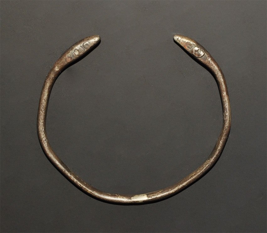 Near Eastern Silver Snake-Heads Bracelet: 4th-2nd century BC. A round-section penannular bracelet with thickened finials, lozengiform in profile, each with punched ring-and-dot eyes, hatched texture to the upper body. 23 grams, 73 mm (3"). Pr