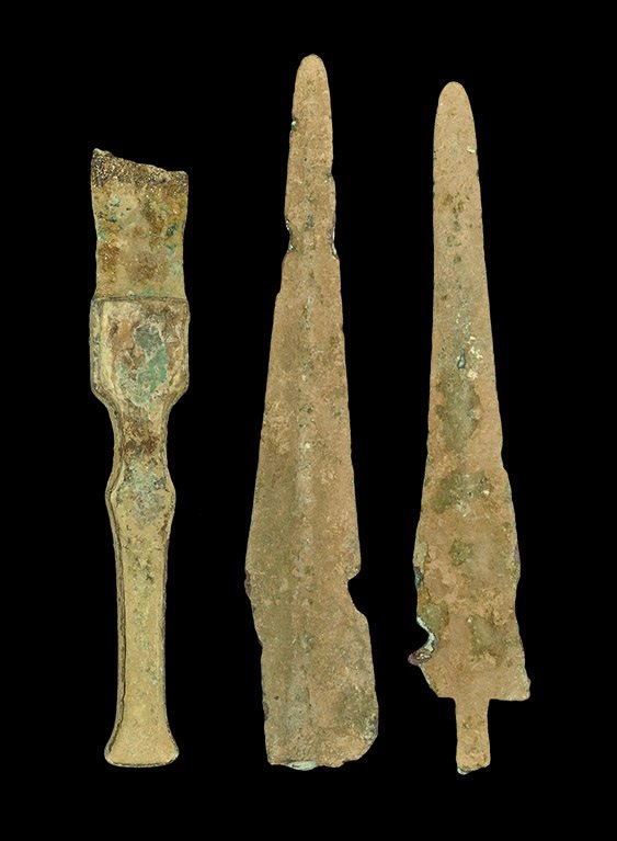 Near Eastern Luristan Bronze Weapon Group: 2nd millennium BC. A mixed group of Bronze Age weapons comprising: a waisted sword-hilt with lateral flanges to both faces, upper end of blade; a broad triangular lentoid-section spearhead; a narrow t