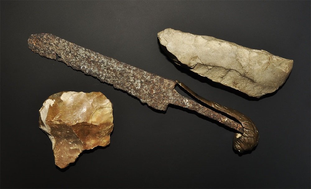 Post Medieval and Stone Age Axe and Dagger Group: A mixed group comprising: a Neolithic polished stone axe with square butt; a19th century sabre hilt and cut-down single-edged blade, lion-head finial. 836 grams total, 9-28 cm (3 1/2 - 11"). Ex Goslin