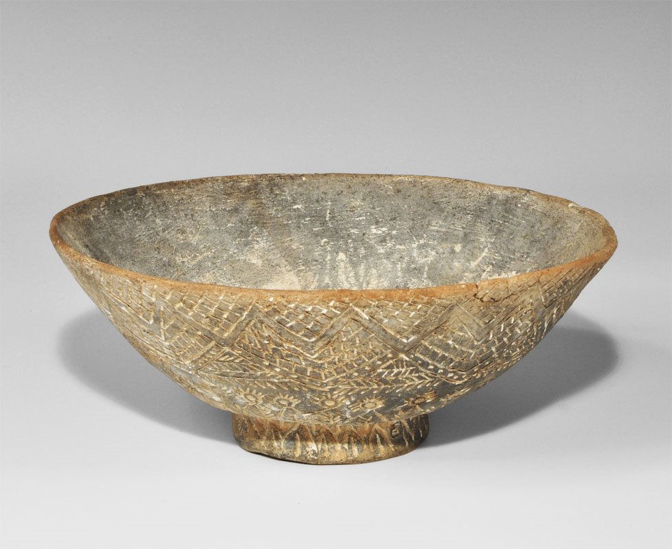 Near Eastern South Arabian Incised Dish: Circa 2nd century AD. A broad terracotta bowl with black surfaces, flared base; incised ornament to the outer face, chevrons, zigzags and hatched panels above a band of rosettes, hatching below. From