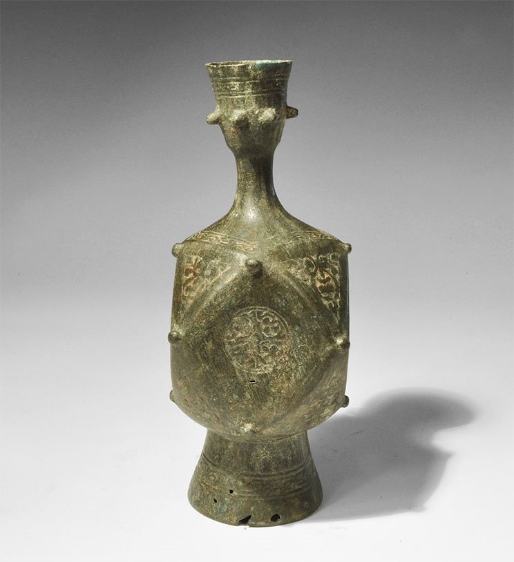 Islamic Bronze Polyhedral Vessel: 13th-15th century AD. A hollow vessel with facetted body, flared conical base and tubular neck with funicular top, flared rim; the base open with decorative band; knop to each angle of the body, roset