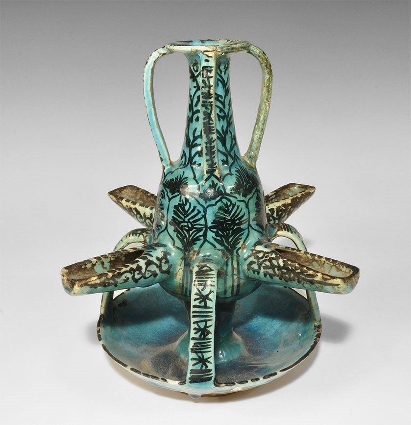 Islamic Glazed Ceramic Oil Lamp: 18th century AD. A blue-glazed lamp comprising a broad bowl with central vertical column, bulb with four flat-section straps to the rim of the bowl and four deep nozzles; conical neck with flared rim 