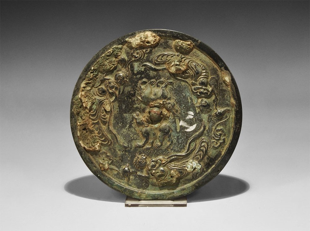 Chinese Bronze Zoomorphic Mirror: Han Dynasty, 206 BC-220 AD. A cast discoid mirror with one polished surface; to the reverse a pierced bulb with two bears flanking, outer band of bird-headed human figures. Ex McQuinley collection, ac