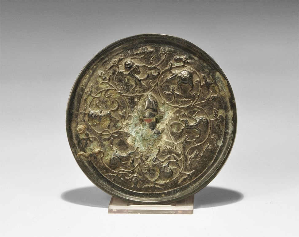 Chinese Bronze Monkeys and Grapes Mirror: Han Dynasty, 206 BC-220 AD. A cast discoid mirror with one polished surface; to the reverse a pierced bulb in the form of a monkey surrounded by a frieze of monkeys amid vegetation. Ex McQuinley colle