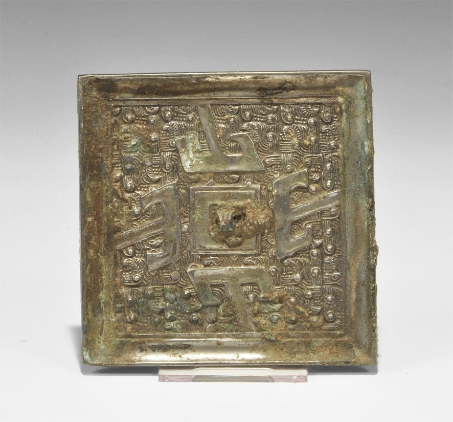 Chinese Bronze Geometric Mirror: Han Dynasty, 206 BC-220 AD. A small cast square mirror with one tinned and polished surface; to the reverse, a central pierced lug with four tau-shaped arms on a hatched field. Ex McQuinley collection