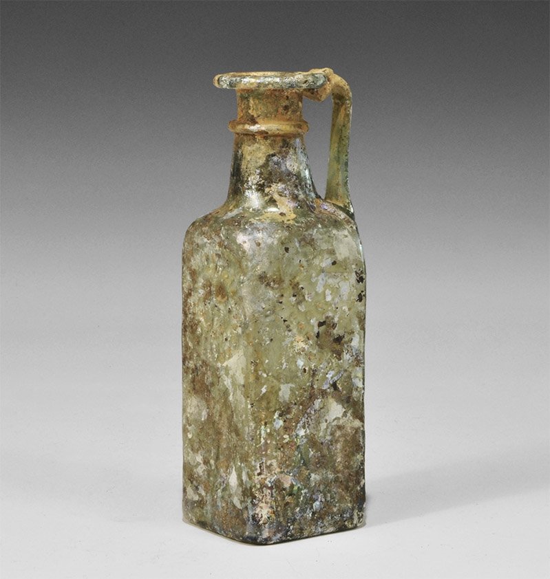 Byzantine Glass Four-Sided Jug with Christian Symbols: 6th-9th century AD. A square-section jug with conical neck, everted rim, applied trails to rim and neck, some iridesence; applied trail handle to the shoulder; to two faces, an arch with lozenge and i