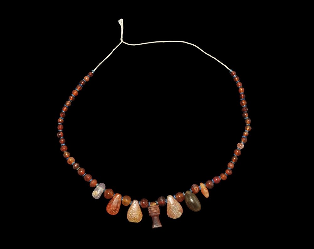 Egyptian Carnelian Djed Pillar Bead and Pendant Group: Saite Period, 624-525 BC. A restrung group of graduated globular carnelian beads, glazed composition discoid beads, crystal and carnelian teardrop pendants, carnelian djed pillar pendant. Acquired on 