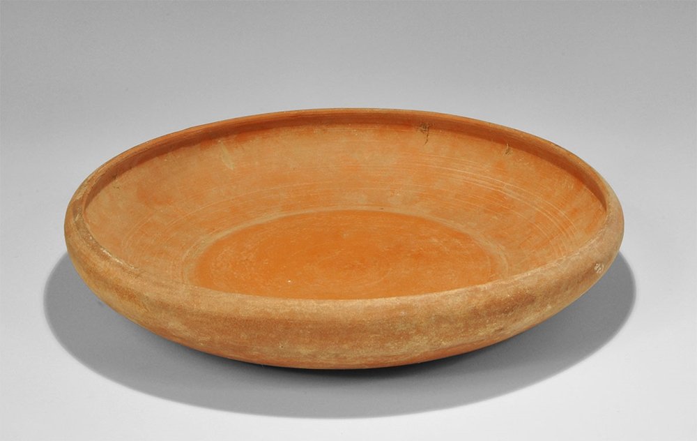 Roman Redware Broad Bowl: 1st-3rd century AD. A large terracotta bowl with flat base, rounded wall and inturned rim; North African origin. From an important London collection, acquired in the 1970s. 1.2 kg, 30.5 cm (12"). Time