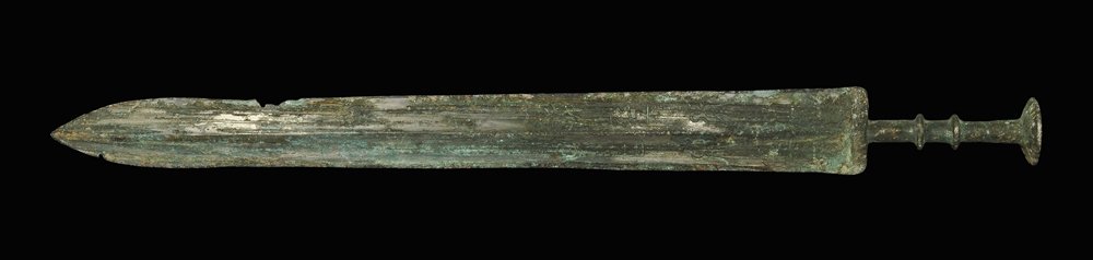 Chinese Bronze Epigraphic Sword: Han Dynasty, 206 BC-220 AD. A short sword with midrib to the gently waisted blade; elliptical guard, two transverse discoid collars to the grip and large discoid pommel above; the blade with two colum