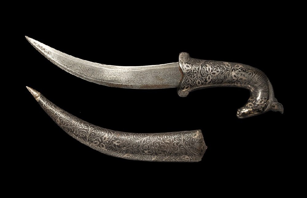 Indian Qajar Style Jambiyya Dagger: An undated archaistic jambiyya with curved blade, lined scabbard and zoomorphic hilt; the grip and scabbard with etched running foliage ornament, the pommel a horse-head. 343 grams, 33 cm (13"). From 