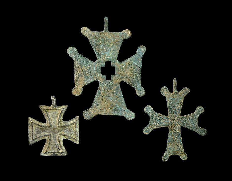Byzantine Style Bronze Pectoral Cross Pendant Group: A mixed group of undated archaistic cast cruciform pendants comprising: a bifacial Maltese cross with raised inner border; an expanding-arm cross with lobes to the corners, central cruciform void and 