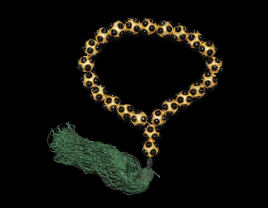 Islamic Glass Prayer Bead Necklace with Tassel: A restrung necklace of undated archaistic white metal spherical beads each with two rows of black glass cabochon eyes with ropework collars; green fabric tassel. 105 grams, 34 cm (10 cm internal diame