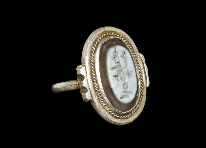 Islamic Stone Intaglio in a Modern Silver Finger Ring: An undated archaistic banded agate intaglio with calligraphic text set in an elliptical bezel, round-section hoop to the underside. 9.69 grams, 28 mm overall, 19.92 mm internal diameter (approximate s