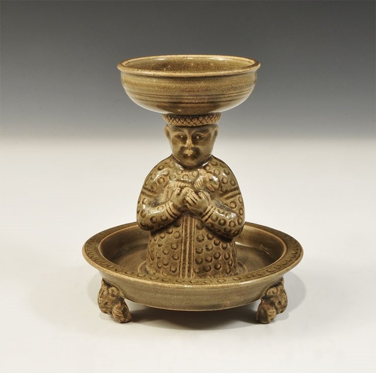 Cambodian Style Glazed Ceramic Incense Burner: An undated archaistic green-glazed incense burner comprising a broad tray with three zoomorphic feet, stem formed as a male figure holding a lamb in his arms, upper bowl with everted rim. 580 grams, 1