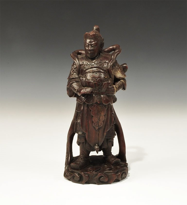 Chinese Wooden General Figurine: 19th century AD. A carved figurine of an armoured soldier on a discoid base with scroll detailing; the figure with heavy boots, open-fronted coat, layers of lacquered armour, helmet with plume. 558 gr