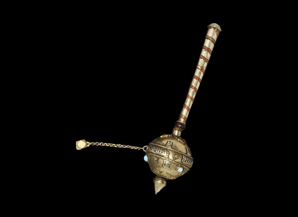 Chinese Tibetan White Metal Prayer Rattle: 19th-20th century AD. A Buddhist prayer rattle comprising a tubular handle with spiral-bound copper strip, hollow bulb head on a wooden bearing and knop finial; the head with appliqués of foliage, in