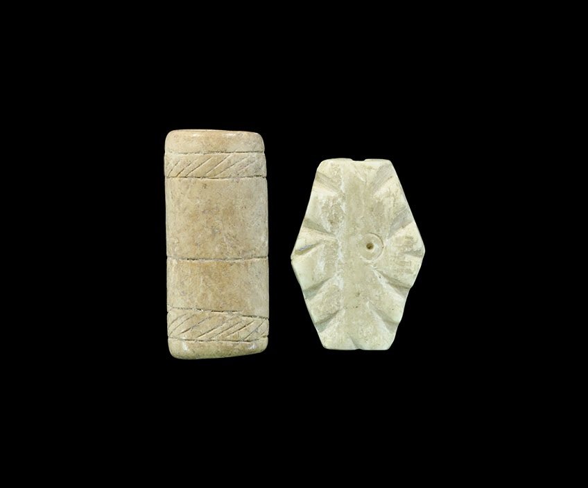 Near Eastern Bone Bead Group: 1st millennium AD. A group of two carved bone beads comprising: one flat, lozengiform with ring-and-dot to each face, notched edges; an elliptical-section tube with bands of hatching to the edges, inc