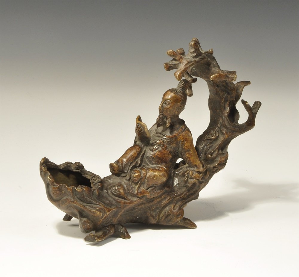 Chinese Style Bronze Reclining Scholar Incense Burner: 20th century AD. A hollow-cast figurine of a scholar reading, reclining against a tree; the lower end a bowl to accept incense. 547 grams, 16.5cm (6 1/2"). Property of a gentleman; acquired in the 199