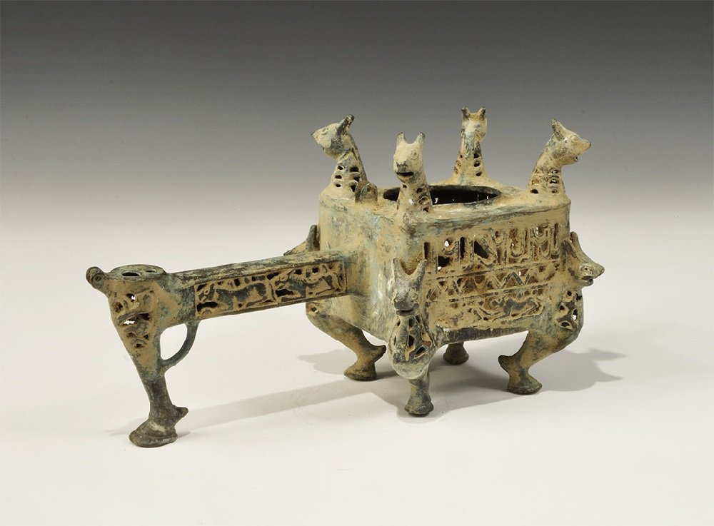 Islamic Seljuk Style Bronze Incense Burner: An undated archaistic openwork hollow-cast burner, square in plan with zoomorphic foot to each corner and head to the rim; rectangular-section openwork handle with supporting leg and void above with h