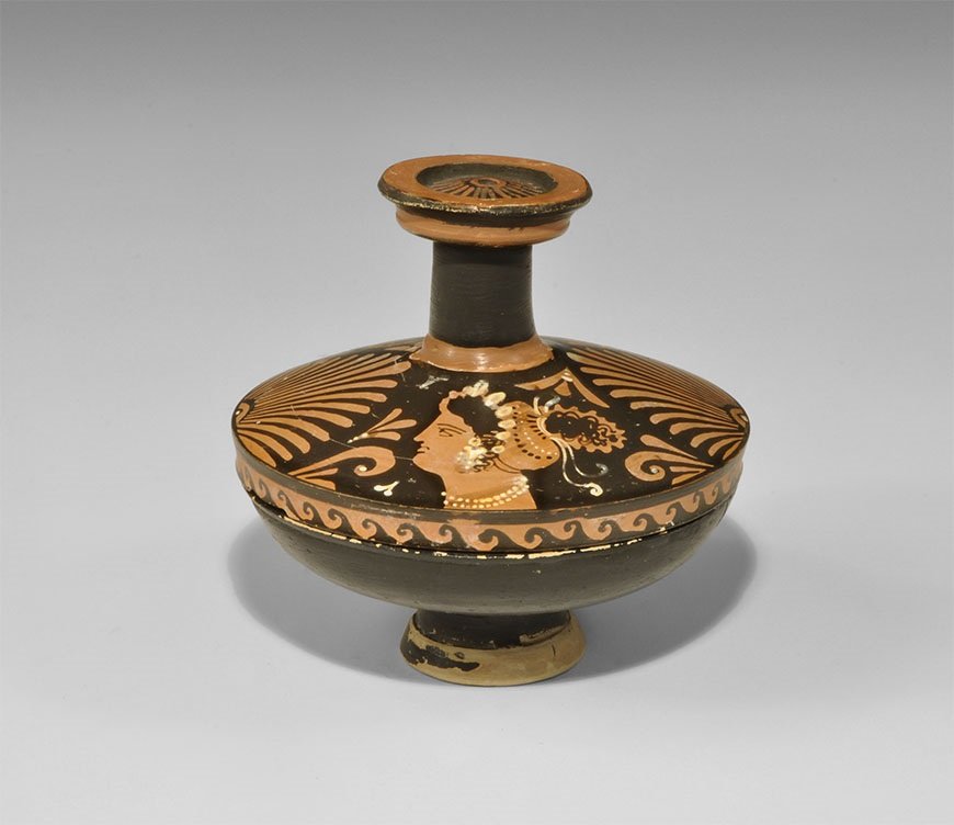 Greek Apulian Painted Ceramic Lekanis: 5th-3rd century BC A blackware lekanis with pedestal foot, lid with tall discoid handle; the handle with red bands and central rosette, the lid with palmettes and ladies of fashion with restrained whi
