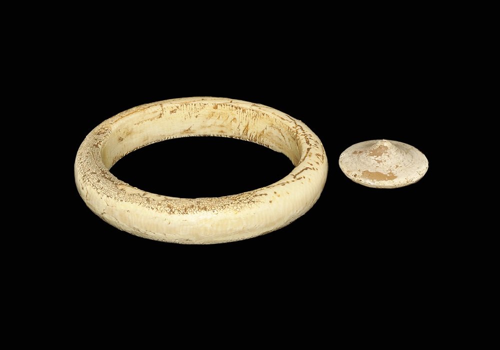 Bronze Age Ivory Carved Bangle and Shale Button Group: 2500-500 BC A mixed group of items comprising: a carved D-section annular bangle; a discoid fastener with conical profile to the upper face, pierced to the underside. Cf. carved shale buttons from Dor