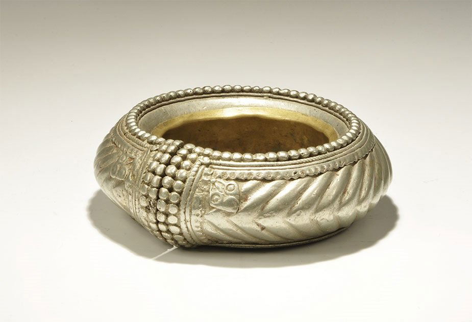 Ethnographic White Metal Anklet Ashtray: 20th century AD. An ashtray formed by inserting a brass tray into a large white-metal biconical penannular anklet with pelletted upper rim and borders, chevron ribbing to the outer face, lozenge plaqu