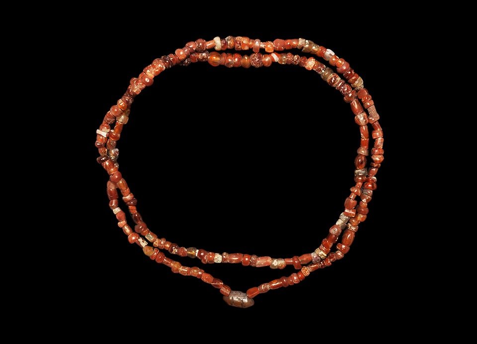 Roman & Near Eastern Carnelian Bead String: 1st century BC and later. A restrung loop of mixed small excavated carnelian beads featuring an Islamic prayerbox-shaped pendant; bead-shapes include spheres, ovals, biconical barrels, oblates, facett