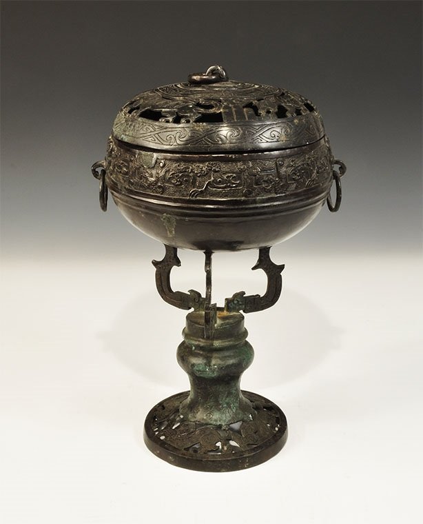 Chinese Style Bronze Lidded Incense Burner and Stand: An undated archaistic cast incense burner with band of Han Dynasty style ornament to the shoulder, two suspension rings to the sides, integral stand comprising an openwork discoid base with running dr