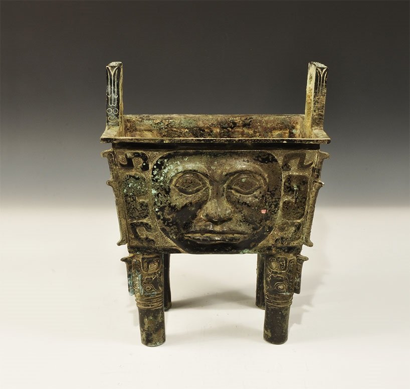 Chinese Style Bronze Fang Ding Vessel: An undated archaistic cast food vessel, rectangular in plan with everted rim and four cylindrical legs; to each face a human mask and geometric design extending to the upper legs, flange to each corne