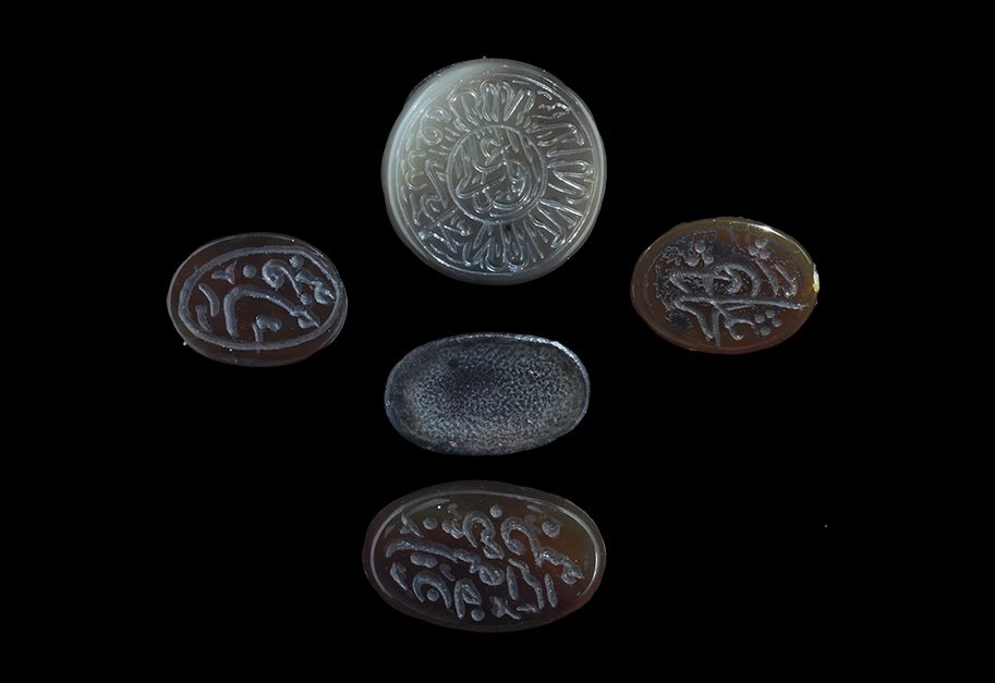 Islamic Style Hardstone Inscribed Intaglio Group: A mixed group of undated archaistic carved intaglios comprising: one discoid, grey, calligraphic text to upper face; four elliptical, brown-ochre, calligraphic text to upper face. 13 grams total, 18-2