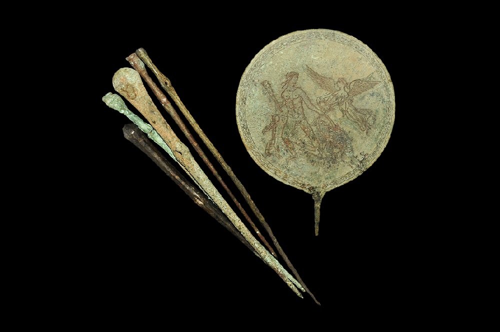 Near Eastern Bronze Mirror & Pins Group: 1st millennium BC. A mixed group of cast bronze items comprising: an Etruscan style discoid hand-mirror with low-relief scene of Hercules slaying the Cretan bull with his club; two large pins each wit