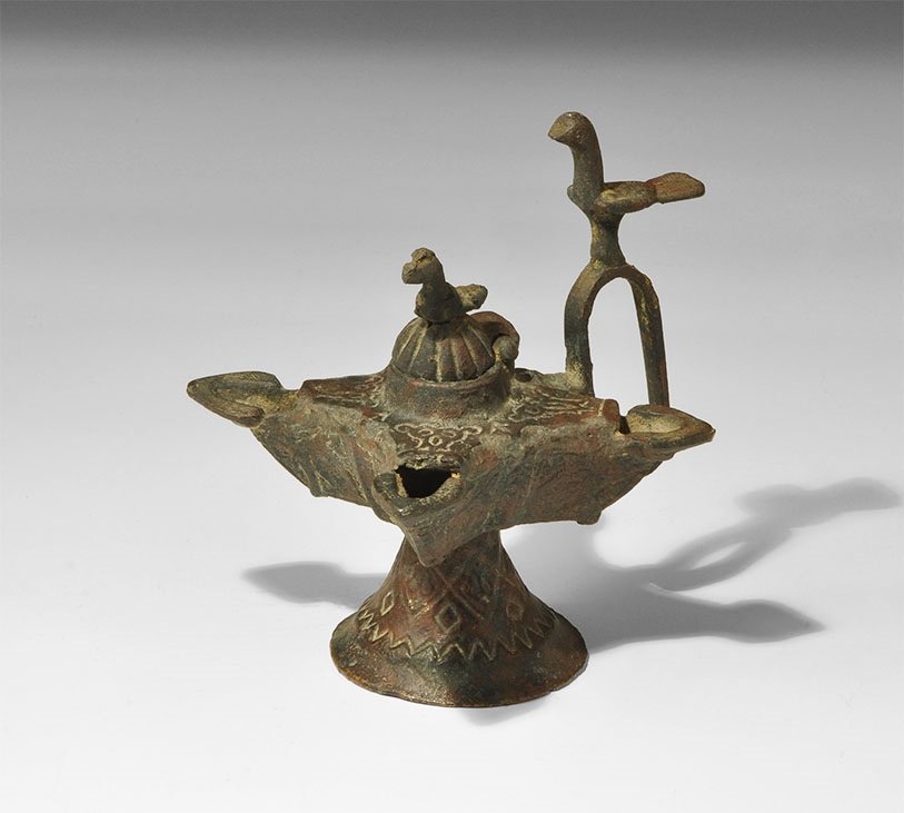 Islamic Bronze Khorasan Multi-Spouted Oil Lamp: 12th century AD. A hollow-cast lamp with flared base, cruciform body and hinged lid; the base with incised geometric ornament, the body with four spouts, each with a leaf-shaped lip, arabesque ornamen